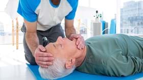 Patient on floor about to receive CPR from man kneeling at his side with emergency oxygen cylinder in the background